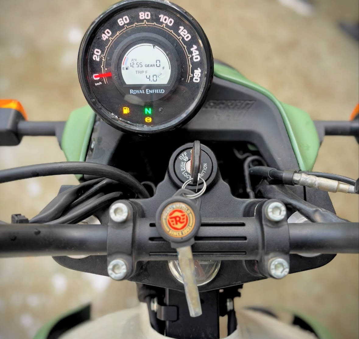 Royal Enfield handlebar and analogue speedometer with digital trip display seen from the rider's seat on a green fuel tank